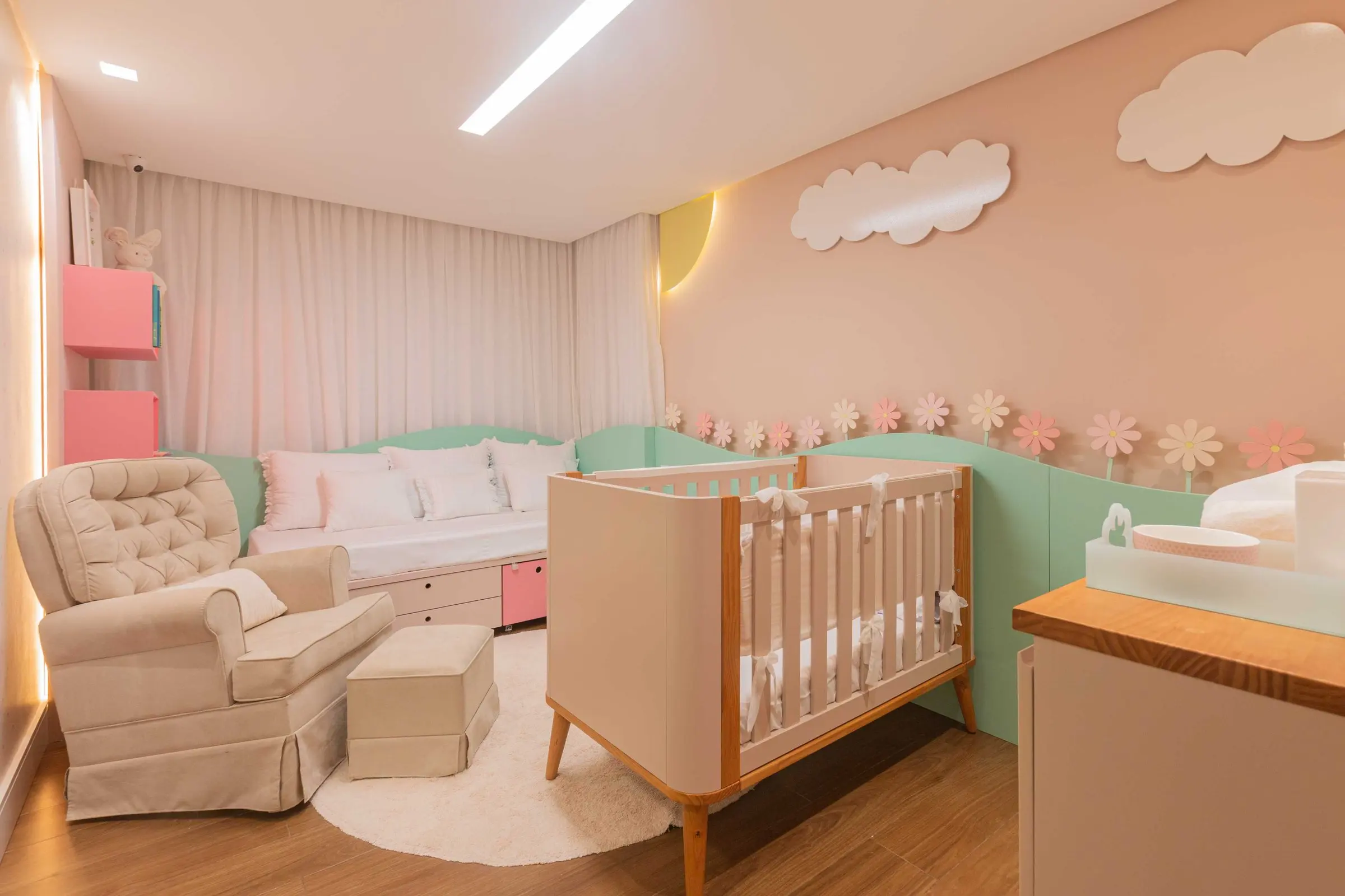 Quarto de bebê rosa com nuvens na parede, berço e poltrona de amamentação