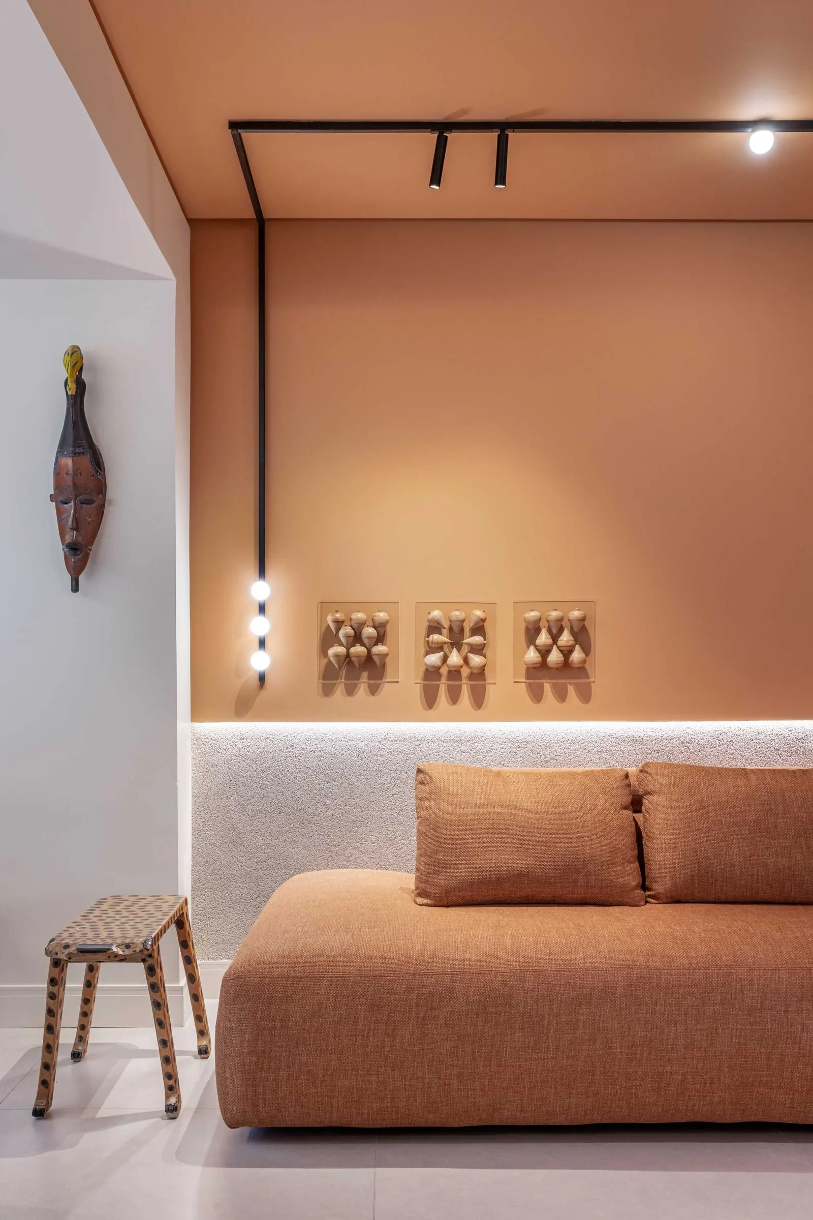 Terracotta sofa under track lighting with decorative wall pieces
